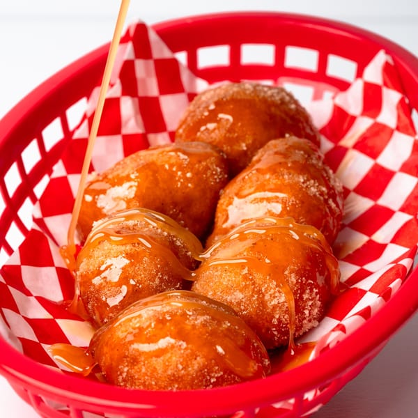 Shawarma Shack's golden-brown fried dough balls, drizzled with sweet syrup, in a red checkered basket.