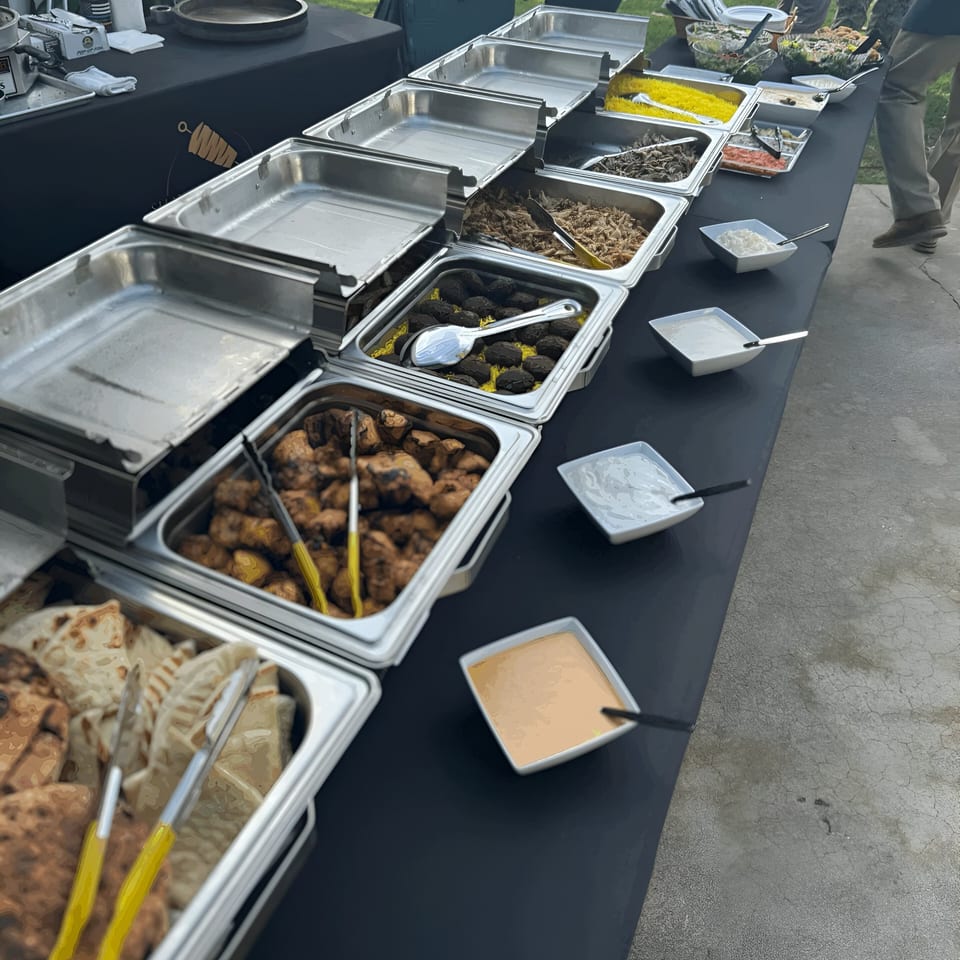 A buffet line of Mediterranean food, including rice, falafel, chicken, and pita bread, with sauces.