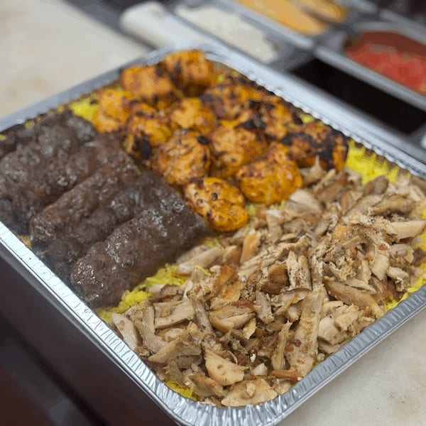 A Shawarma Shack platter with yellow rice, chicken shawarma, kofta, and chicken tikka in a foil tray.