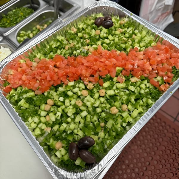 A large catering tray of Mediterranean salad with diced cucumbers, tomatoes, chickpeas, and olives.
