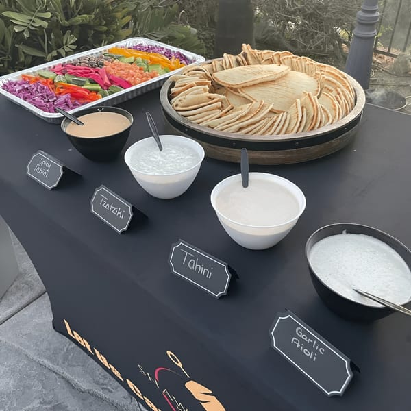 A Shawarma Shack catering spread with pita bread, fresh vegetables, and various Mediterranean dips.