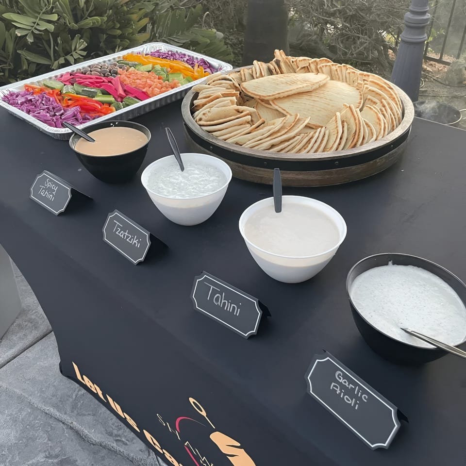 A Shawarma Shack catering spread with pita bread, fresh vegetables, and various Mediterranean dips.