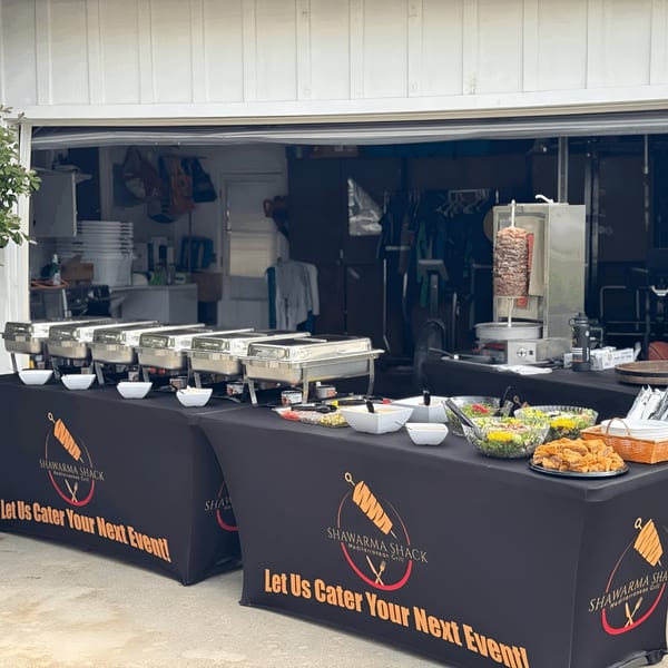 Shawarma Shack catering setup with chafing dishes, salads, and a vertical rotisserie for shawarma.