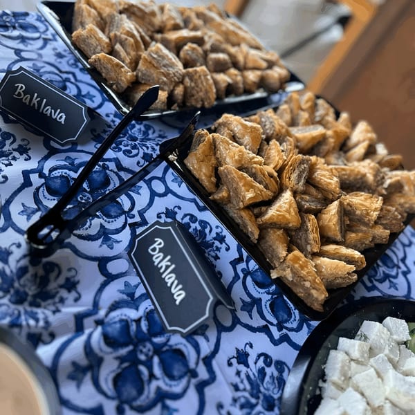 Trays of golden baklava pastries and white Turkish delight cubes on a blue and white patterned tablecloth.