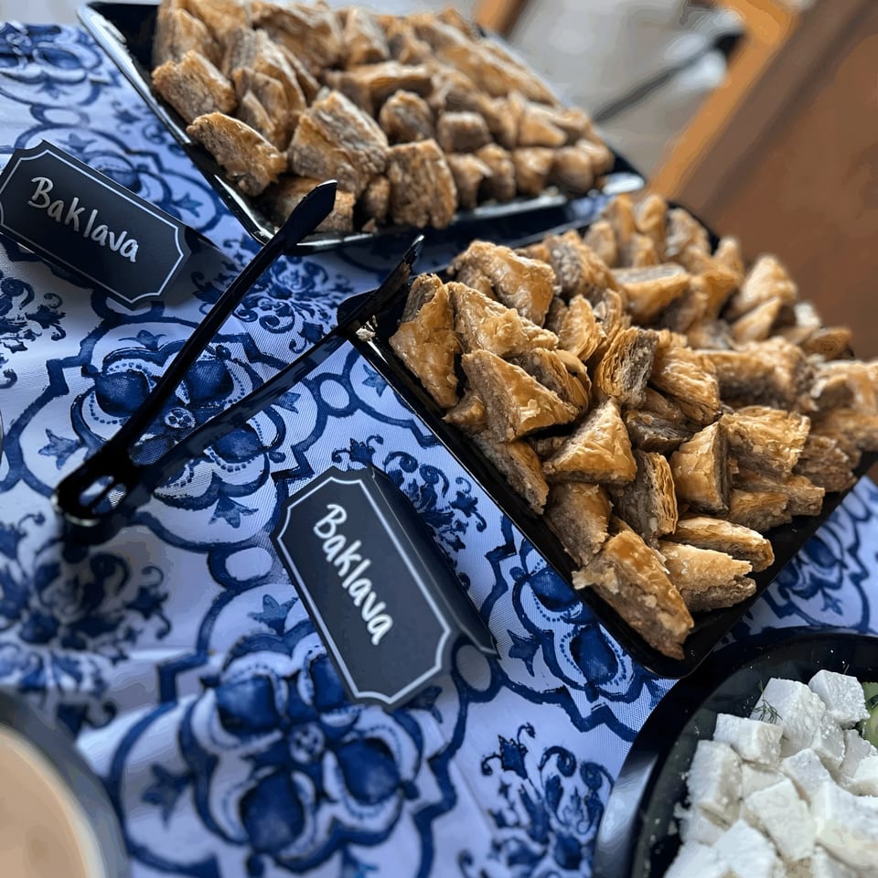 Trays of golden baklava pastries and white Turkish delight cubes on a blue and white patterned tablecloth.