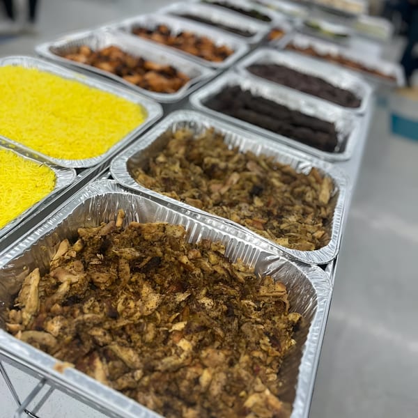 Several foil trays of Mediterranean food, including yellow rice, shawarma, and dark meat.