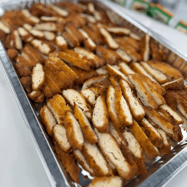 A catering tray filled with golden-brown, breaded chicken cutlets, sliced into strips, ready to serve.